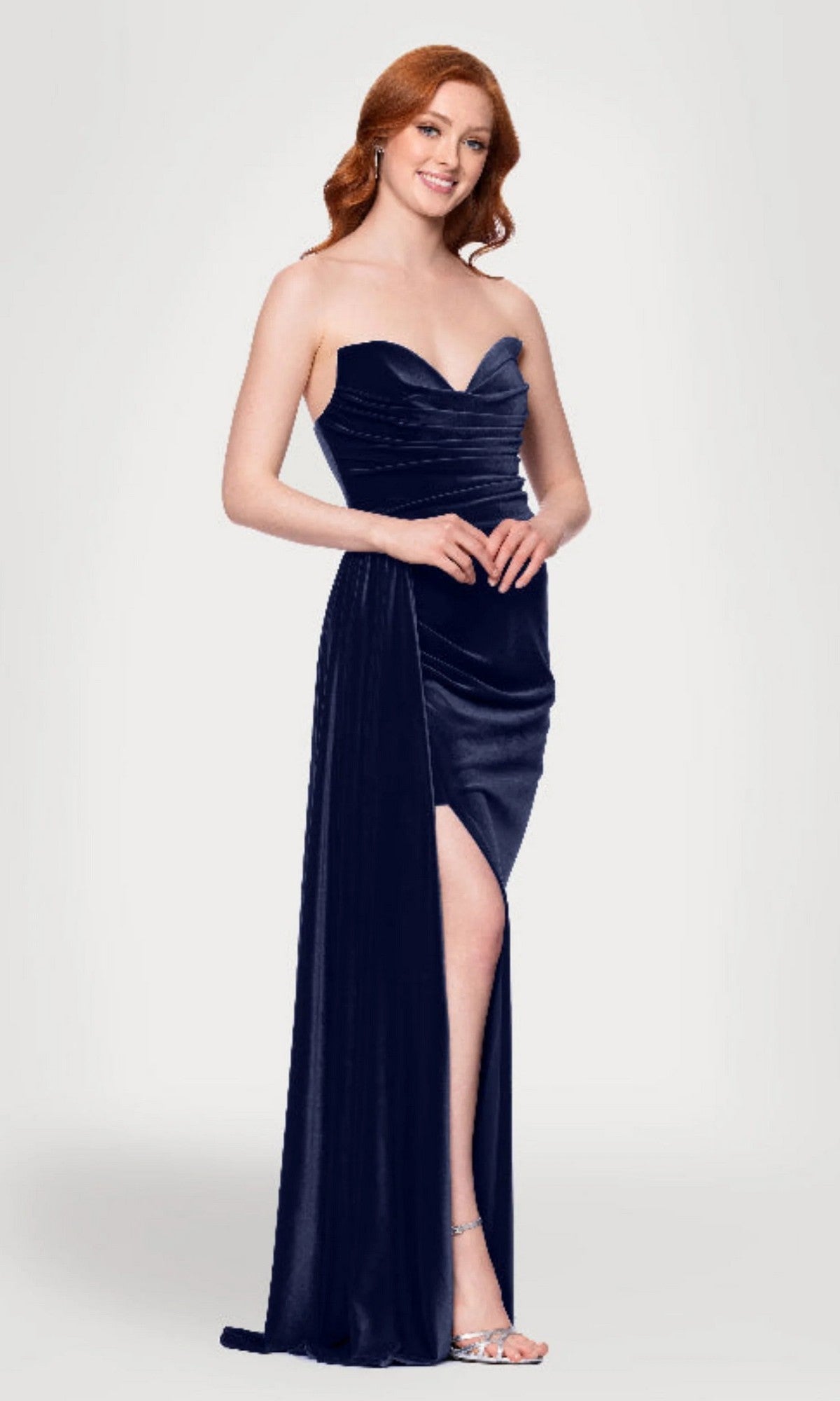 A woman in a navy Blondie Nites 5138BN long prom dress with a strapless sweetheart neckline and thigh-high slit stands against a plain light background.